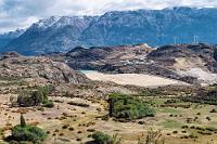 Cerro Bayo Project  Wir sind nur noch 25 Kilometer von der Grenze entfernt, als uns der "Mirador Laguna Verde" zu einem letzten Stop auf chilenischer Seite einlädt. Vom Parkplatz an der Straße führt ein kurzer Pfad zu einem überdachten Pavillion am Hang über einer kleinen Halbinsel, von dem aus man auf zwei sehr unterschiedliche Lagunen schaut. Linker Hand liegt ein kleiner Abraumsee unterhalb mehrerer Gebäude, in denen das "Cerro Bayo" Abbauprojekt einer Minengesellschaft residiert. Verteilt über das Gelände der ganzen Halbinsel gibt es sowohl einen Tagebau, sowie mehrere Untertageminen, in denen u.a. zwischen 1995 und 2017 45 Mio. Unzen Silber sowie 650.000 Unzen Gold gefördert wurden. Dass die einzigen drei Windräder, die wir auf unserer Reise gesehen haben, ausgerechnet auf dem Gelände einer kanadischen Minengesellschaft stehen, läßt sie beinahe nach einem umweltpolitischen Ablass aussehen.