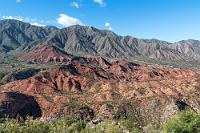 Sierra Los Colorados  Wir haben die Passhöhe, den "Punto Alto" mit 2040 m, überquert und es geht in Serpentinen wieder bergab. Neben der Straße befindet sich die Ausweiche "Mirador Miranda", wo wir die Gelegenheit wahrnehmen, ein paar Fotos der auch hier noch dominierenden roten Felslandschaft aufzunehmen. Unten im Tal fließt ein kleines Flüsschen, dem die Straße und auch wir folgen.
