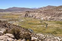 Río Isluga  Der Fluß, der durch die malerische Landschaft des Nationalparks Volcán Isluga fließt, entspringt der 4147 m hoch gelegenen Laguna Parinacota in der Nähe des Vulkans.  Wir haben spritsparend ca. einen halben Tag bewegungslos auf diesem Parkplatz oberhalb des Flusses verbracht, darauf wartend, am Abend von der freundlichen Hoteliersschwägerin mit dem für die Weiterreise dringend benötigten Benzin versorgt zu werden.  Verblüfft waren wir allerdings, als sich das einzige an diesem Tag hier auftauchende Fahrzeug als ein Polizeijeep entpuppte, der noch dazu direkt neben uns stehen blieb. Noch verblüffter, als die beiden Beamten uns durch das heruntergekurbelte Fenster fragend mit unserem Namen begrüßten! Es stellte sich heraus, dass uns durch eine Fehlbuchung der Reiseagentur ein weiteres Zimmer im einzigen anderen Hotel Colchanes angemietet worden war – was wir nicht wußten! Der besorgte Hotelier hatte vorsorglich die Polizei alarmiert, als wir nicht zum gebuchten Termin auftauchten – schließlich hätten wir auf der abgeschiedenen Tour durch das Hochland liegen geblieben sein können. Soviel Sorge um unser Wohlergehen hat uns gerührt und nach ein paar erklärenden Worten und einem Dankeschön an den vorsorglichen Hotelier konnte das Mißverständnis geklärt werden.