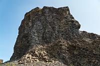 Basalt Mikado  Auf halber Strecke zur Ásbyrgi Schlucht lädt ein Abstecher zum Besuch des 'Echofelsens' Hljóðaklettar ein. Von einem etwa zur Hälfte gefüllten Parkplatz folgen wir einem schmalen Pfad durch lichten Birkenbewuchs und gelangen nach einigen hundert Metern zu einer Ansammlung von Basaltklippen, die sich entlang des Flusses Jökulsá á Fjöllum erstreckt. Gleich an der vorderen Front erhebt sich ein Felsen, der wieder sämtliche Spielarten von Basaltsäulen und -rosetten aufweist.  Auf der gegenüberliegenden Seite des Flusses erstreckt sich eine wie aufgeschüttete Kohleberge aussehende Hügelkette, deren in den Fluß ragender Ausläufer ebenfalls aus vielfach verknoteten Basaltformationen besteht.