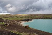 Entwarnung  Nix mit Sensationen! In dem sich aktuell in hellem Sonnenlicht darbietenden Grindavík mit seinem harmlosen Kleinstadtcharakter angekommen, verlassen wir die Küstenstraße für ein paar Kilometer Richtung Norden ins Hinterland, wo es am ehesten Zeugnisse der Ausbrüche zu sehen geben sollte. Die gibt es auch in Form von riesigen pechschwarzen Aschehügeln, die in der ohnehin gebirgig werdenden Landschaft meterdick die Hänge bedecken. Dort allerdings, wo wir aus der Ferne Dampfsäulen gesehen hatten, befinden sich am Boden wieder nur Kraftwerks- und Industriegebäude, aus deren Schornsteinen die Überbleibsel der genutzten Wärmeenergie entweichen.  Etwas enttäuscht ob unserer hochgeschraubten Erwartungen verlassen wir den Ort bald wieder. Nach etwas über 20 km auf der 427 biegen wir jedoch für ein paar Kilometer nach Norden auf die 42 ab, denn hier verspricht der Reiseführer eine verläßlichere Sehenswürdigkeit. Zuvor lockt aber der rechts neben der Straße liegende Grænavatn mit seiner leuchtend grünen Farbe zu einem Kurzhalt.