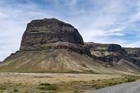 Lómagnúpur  Kurze Zeit darauf sind wir wieder auf der 1, begleitet von kargen Lavafeldern und flachem Weidegrund, der sich bis zum Meer erstreckt. Wir nähern uns dem ausgedehnten Schwemmsandgebiet des Flusses Núpsvötn, der hier ein breites Delta geschaffen hat. Wir halten auf einem Rastplatz direkt am Fuße des Lómagnúpur, dem südlichsten Ausläufer eines Bergzuges, welcher sich vor 2,5 bis 1,5 Mio. Jahren aus sogenanntem Palagonit, Lavagestein und Sedimenten aufgelagert hat. Die steilen Klippen dieser domförmigen Bergspitze, an denen während mehrerer Eiszeiten das Meer etliche Spuren hinterlassen hat, sind mit 670 m Höhe die höchsten auf Island.  Eine weitere Skurrilität bildet eine moderne, auf acht schlanken Betonstümpfen ruhende Brücke, die ohne ausgebaute Auffahrten wenige Meter rechts der aktuellen Flussquerung der Nationalstraße 1 den Núpsvötn überspannt. Spontan fühlen wir uns an ähnliche Bauwerke in Deutschland erinnert, die ebenfalls seit Jahren als Folgen alltäglicher Fehlplanung mitten in der Landschaft stehen ;-).