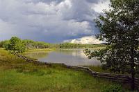 Sonnenflecken  Noch vor dem Erreichen des Green Lake passieren wir einige kleinere Seen, deren sonnenlichtgestreifte Ufer unter dem Gewitterhimmel so reizvoll aussehen, dass wir am liebsten alle paar Meter für ein Foto angehalten hätten. Als wir am Green Lake ankommen und ihn auf einem 15 km langen Uferstraßenabschnitt begleiten, ist das Gewitter schon fast abgezogen und nur noch der nasse Straßenbelag erinnert an den kürzlichen Guss. Da, wo die Sonne Flecken auf dem Wasser bildet, erahnt man das wirklich bemerkenswerte Grün des "Green Lake", es ist aber, aus dem flachen Winkel von der Uferstraße aus betrachtet, längst nicht so beeindruckend wie die Lichtstimmung an den kleinen Seen zuvor. Wir verlassen das Seeufer und biegen nach Lone Butte ab, erreichen den HWY 24 und haben es nun nicht mehr weit bis zu unserer nächsten Unterkunft am Fawn Lake, die wir über eine Schotterstraße mit großen Regenwasserschlaglöchern ansteuern.