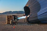 Eingeheizt  Nachdem die großen Körbe von der Hilfsmannschaft von den Trailern gehoben und die Ballonhüllen flach in der Wüste ausgelegt wurden, dürfen wir Passagiere uns nun dem Geschehen nähern. Zaghaft erhellt erstes Dämmerlicht den Horizont und wir beobachten interessiert, wie der Korb gekippt wird, ein starkes Gebläse Luft zum Aufblähen der Hülle produziert, bis schließlich eine lodernde Gasflamme die einströmende Luft erhitzt.