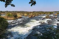 Treppab  Trotz der langen Fahrt haben wir aber noch reichlich Zeit. Wir fahren Richtung Divundu ein Stückchen zurück, biegen nach rechts auf die Brücke über den Okavango, dessen Nordufer hier wieder zu Namibia gehört und folgen dann der Ausschilderung zu den "Popa Falls" einem Feldweg, der natürlich wieder an einem Kassenhäuschen mit Schranke unterbrochen wird. Mit den Tickets haben wir dann immerhin auch gleich den Guide bezahlt, der uns am Parkplatz in Empfang nimmt und uns fürderhin nicht von der Seite weicht. Wir könnten ja die Stromschnellen klauen...