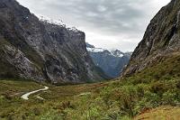 Gate to Milford  Gleich hinter dem Homer Tunnel öffnet sich das Tal, durch welches sich die Milford Road die letzten 20 km bis zum Endpunkt im Sound windet. Dies ist der höchste Punkt der etwas über 90 km langen Sackstraße von Te Anau nach Milford.  Nur wenige Kilometer nach diesem Ausblick von der Paßhöhe, gleich nach den Serpentinen, bietet sich die Möglichkeit zu einer Rast bei "The Chasm", wo man die beeindruckende Kraft des Wassers an ausgewaschenen Steinformationen bewundern kann. So einen denn die Sandflies nicht zum Wahnsinn getrieben haben... ;o) : milford road, te anau, milford sound, homer saddle, homer tunnel, fiordland