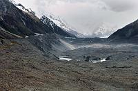 Gletschertreffen  Auch wenn die Bergspitzen fast in der aufliegenden Bewölkung verschwinden, läßt sich gut erkennen, dass der aus der linken Gabelung in das Tasman Valley mündende Tasman Glacier von noch zwei weiteren Gletschern gespeist wird: Aus dem mittleren Tal vom Rudolf Glacier und dem von rechts einfließenden Murchison Glacier. Dieser vereinigte Strom bewegt sich mit immerhin 200 m pro Jahr durch das Tal und löst sich ein paar Kilometer weiter im klimabedingt immer schneller anwachsenden Terminal Lake auf. Unter der nur wenige Meter dicken Geröllschicht ("Oberflächen Moräne"), verbirgt sich an dieser Stelle noch eine gut 200 m mächtige Eisschicht, die allerdings wie fast alle anderen Gletscher weltweit jährlich um etwa 0,5 % abschmilzt. : tasman valley,tasman glacier,terminal lake
