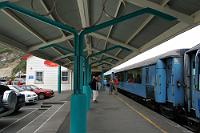 Greymouth Station  Am Ziel- und Umkehrpunkt Greymouth hat der TranzAlpine nur eine relativ kurze Aufenthaltszeit von einer Stunde – nicht genug, um großartige Entdeckungen in der Stadt zu machen. Deswegen macht man die Bahnfahrt auch nicht, sondern wegen der jeweils 4 1/2 stündigen Strecke quer durch die Canterbury Plains, das Alpenvorland, des Anstiegs zum Arthur's Pass, dem nicht enden wollenden 9 km langen Otira-Tunnel und dem Abstieg durch die von Regenwald geprägte Westseite der Südalpen.  Der 28. Dezember 2004 war unser erster Tag nach der Ankunft in NZ und an Bord erfuhren wir, dass die vergangenen sechs Wochen regenmäßig so ziemlich den schlimmsten Sommer seit Menschengedenken markierten. Das Wetter auf dieser Eisenbahnfahrt gab zu Zweifeln an dieser Aussage dann auch wenig Anlaß. Glücklicherweise wurden wir aber ab dem dritten Tag für den gesamten Resturlaub mit den schönsten Sommerwochen verwöhnt ;o). : southern alps, tranz alpine, tranzalpine, kiwirail scenic journeys,greymouth station