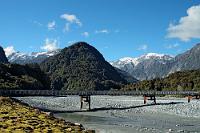 Waiho River  Auch dies ist noch das Gletscherbett des Franz Josef selig. Wenn auch weiter vorne Richtung Tasman Sea. Der vom Gletscher abfließende Waiho River wird mittels dieser Eisengitterbrücke des Highway 6 gequert, welcher einen knappen Kilometer weiter durch das Örtchen Franz Josef führt. Der Blick geht über den Fluß entlang des mittig stehenden Berges auf die Bergkette, welche den Weg zum Gletscher säumt. Wenn man hier steht und von Süden kam, nimmt man Abschied von den Gletschern und freut sich auf die weitere Westcoast mit Hokitika, Greymouth, Punakaiki und Westport. Ganz Abenteuerlustige fahren sogar noch weiter nach Karamea...   Nachtrag 27.03.2019: Sintflutartige Sturzfluten haben heute den größten Teil dieser Brücke hinfort geschwemmt – ein Ereignis, welches umgehend auf  Youtube dokumentiert  wurde und dem Verkehr an der Westküste auf längere Zeit mangels Alternativen mehrere hundert Kilometer lange Umwege aufnötigt. : franz josef glacier, franz josef gletscher, julius von haast, westland, west coast, waiho river, tasman sea