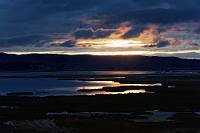 Geschafft!  Müde und erschöpft erreichen wir am Abend unser Hotel in Chucuito. Von unserem Zimmer aus haben wir einen unverstellten Blick auf das Schilfufer einer Titicacabucht und genießen den dramatischen Sonnenuntergang über den Hügeln der vis-a-vis liegenden Landzunge. Im Laufe der heutigen Fahrt haben wir mehrfach kräftige Niederschläge beobachten können, die rund um uns herum aus tiefhängenden Wolken fielen, uns aber nie erreichten. Auch die über dem See aufgezogenen Wolken lassen für den nächsten Tag nicht gerade das Beste erwarten. Andererseits ändert sich das Wetter hier oben so schnell, dass Hoffnung besteht, unsere Titicacasee-Bootsfahrt doch trocken absolvieren zu können. Wir drücken ganz fest die Daumen!