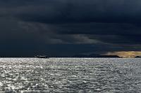 Hübsch grauslig  Auch der schönste Tag geht einmal zu Ende. Vor uns liegt noch die über zweistündige Rückfahrt nach Puno. Wir haben – wie am Vortag herbeigesehnt – ein ausgesprochenes Glück mit dem Wetter gehabt. Den ganzen Tag schien die Sonne und lediglich das quietschfeuchte Schilf auf den Uros-Inseln erinnerte uns daran, welche Güsse noch am Vortag über dem See niedergegangen sind. Wir haben die halbe Strecke zurückgelegt, als sich auch heute abend wieder eine mächtige Front von Südwesten her über den See schiebt. Das tangiert uns jetzt nicht mehr – vielmehr genießen wir das abwechslungsreiche Lichtspiel über dem See – sicher an Bord unseres Bootes, Weltuntergangsstimmung am Himmel.