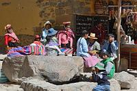 Statisten  Wir verlassen die Festung über den Plaza Manyaraqui, auf dem die allgegenwärtigen Händler plötzlich nicht mehr Mittelpunkt sind, denn aus der gegenüberliegenden "Iglesia de Santiago Apostel" strömt eine  kostümierte Menschenmenge, sammelt sich vor der Kapelle und bewegt sich, nachdem sich die gleich oder ähnlich gewandeten Gruppen sortiert haben über die Brücke des kleinen Flusses in Richtung Ort.